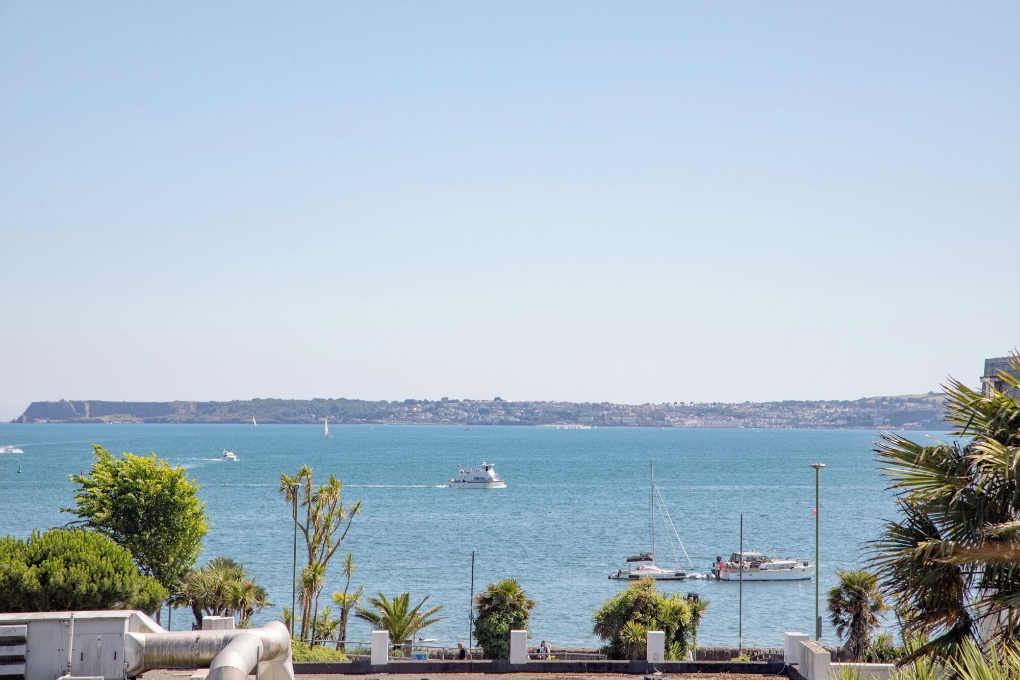 A coastal view with boats on the water, a clear sky, and a distant shoreline with buildings.