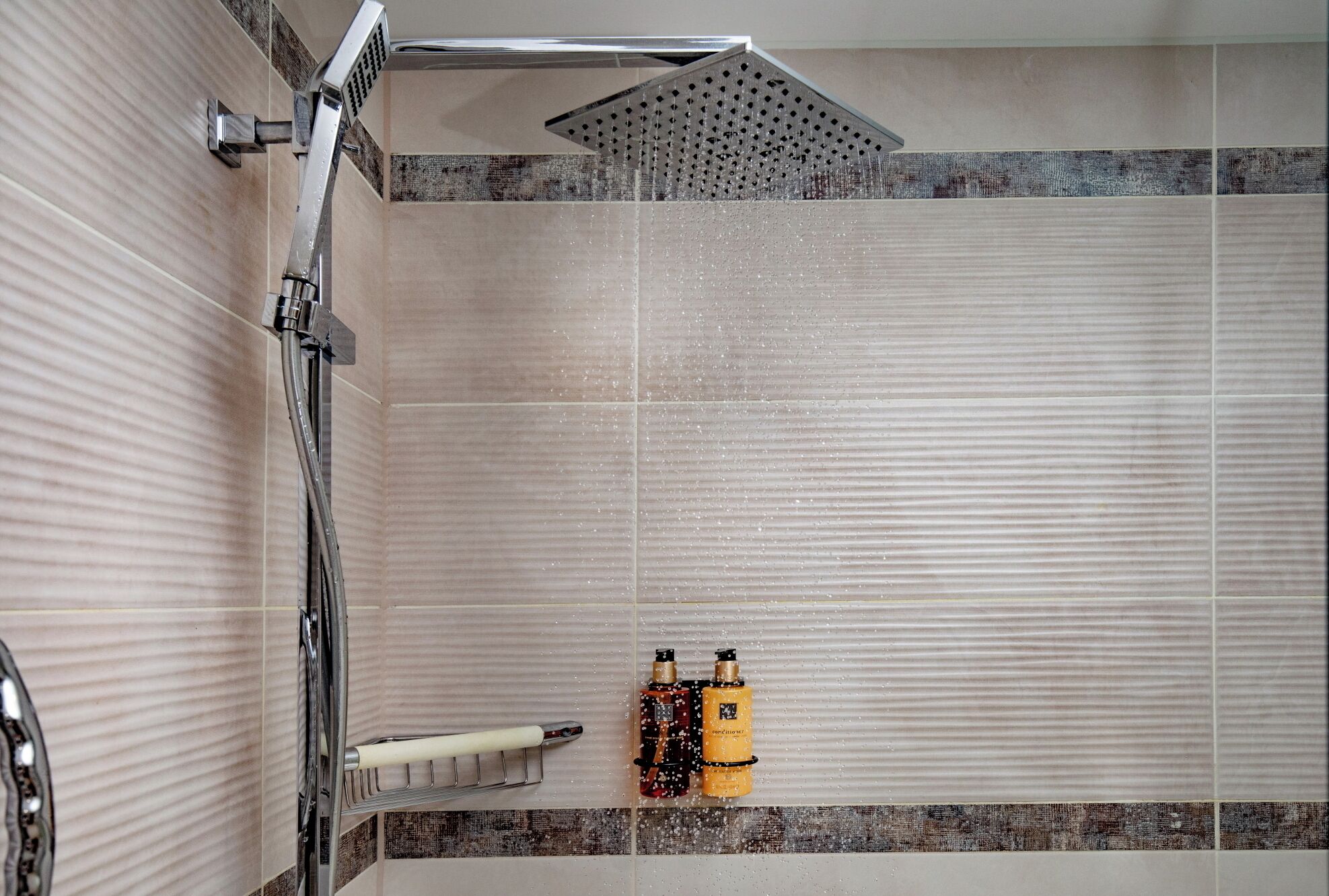 A shower area with a rain showerhead, a towel rack, and two bottles of shampoo.