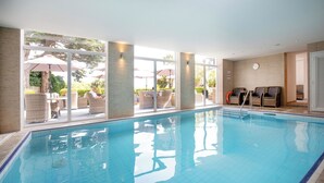 An indoor swimming pool with clear glass walls, wicker furniture, and a view of the outdoors. - Belgrave Sands Hotel & Spa (Torquay)