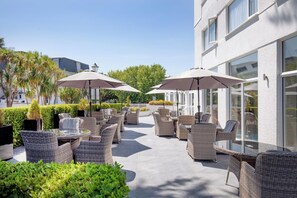 An outdoor patio area with wicker furniture, umbrellas, and a building with large windows. - Belgrave Sands Hotel & Spa (Torquay)