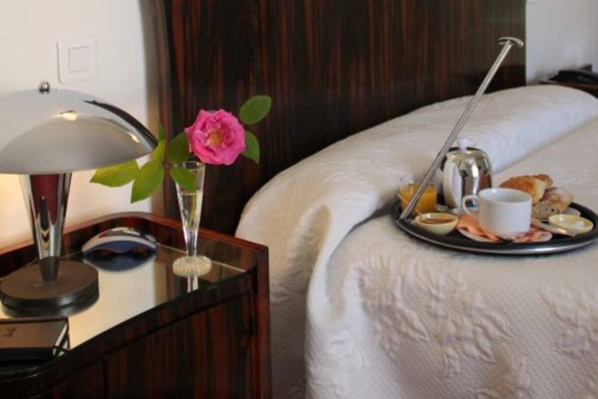 A hotel room with a wooden headboard, a bedside table with a lamp, a tray with breakfast items, and a framed picture on the wall.