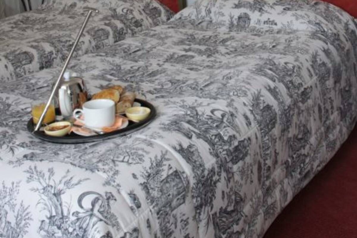A hotel room with two beds, each with a red headboard and a floral-patterned bedspread. There is a tray with breakfast items on the bed.