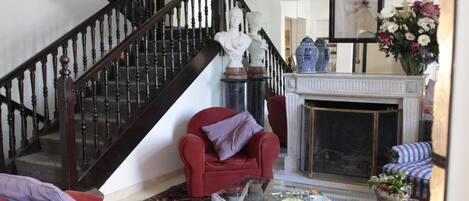 A living room with a red armchair, a glass coffee table with books, a fireplace, and a staircase.
