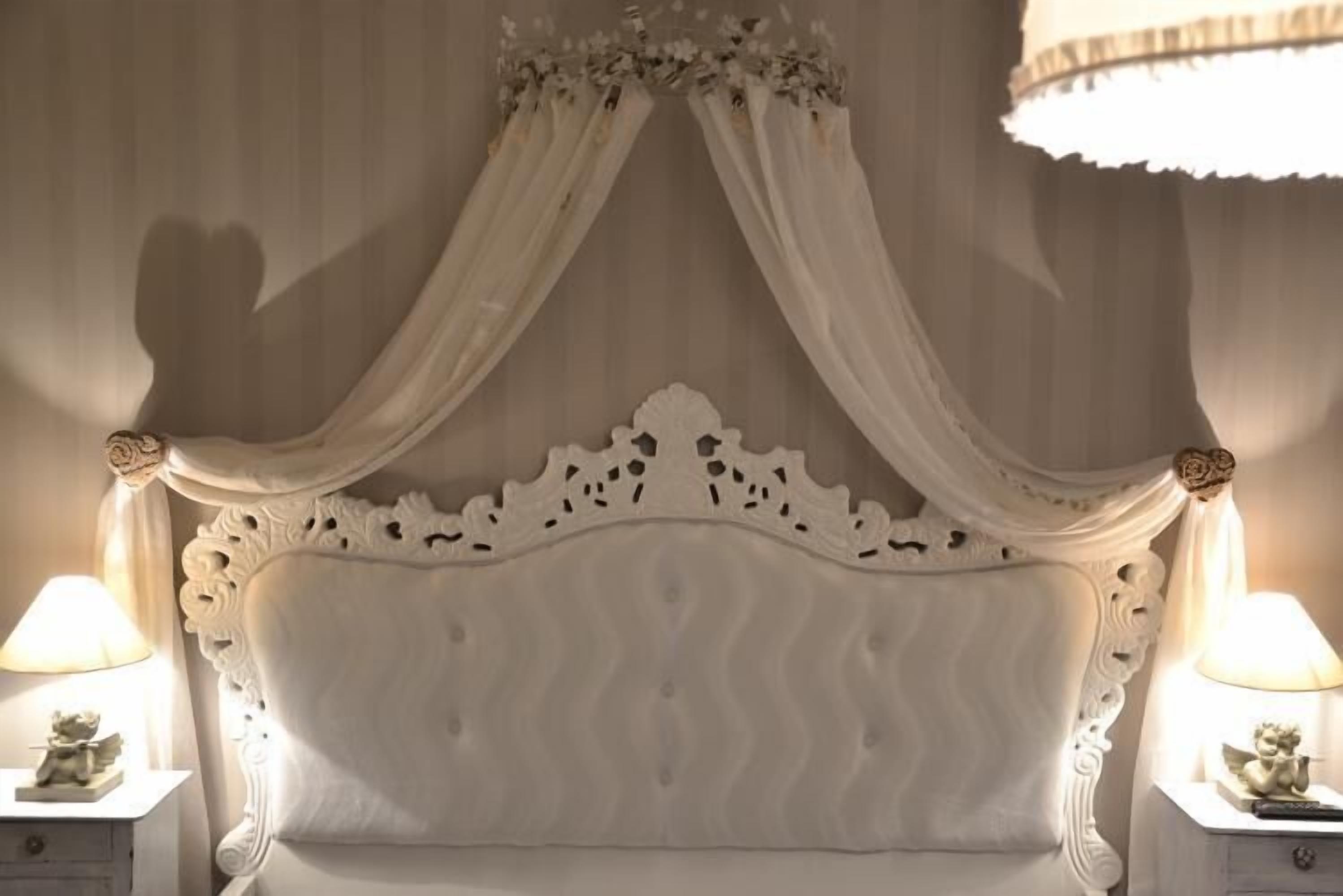 A bedroom with a canopy bed, ornate headboard, and bedside lamps.