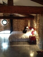 Un dormitorio con techo de madera, un ventanal redondo, una cama, una mesita de noche y una lámpara.