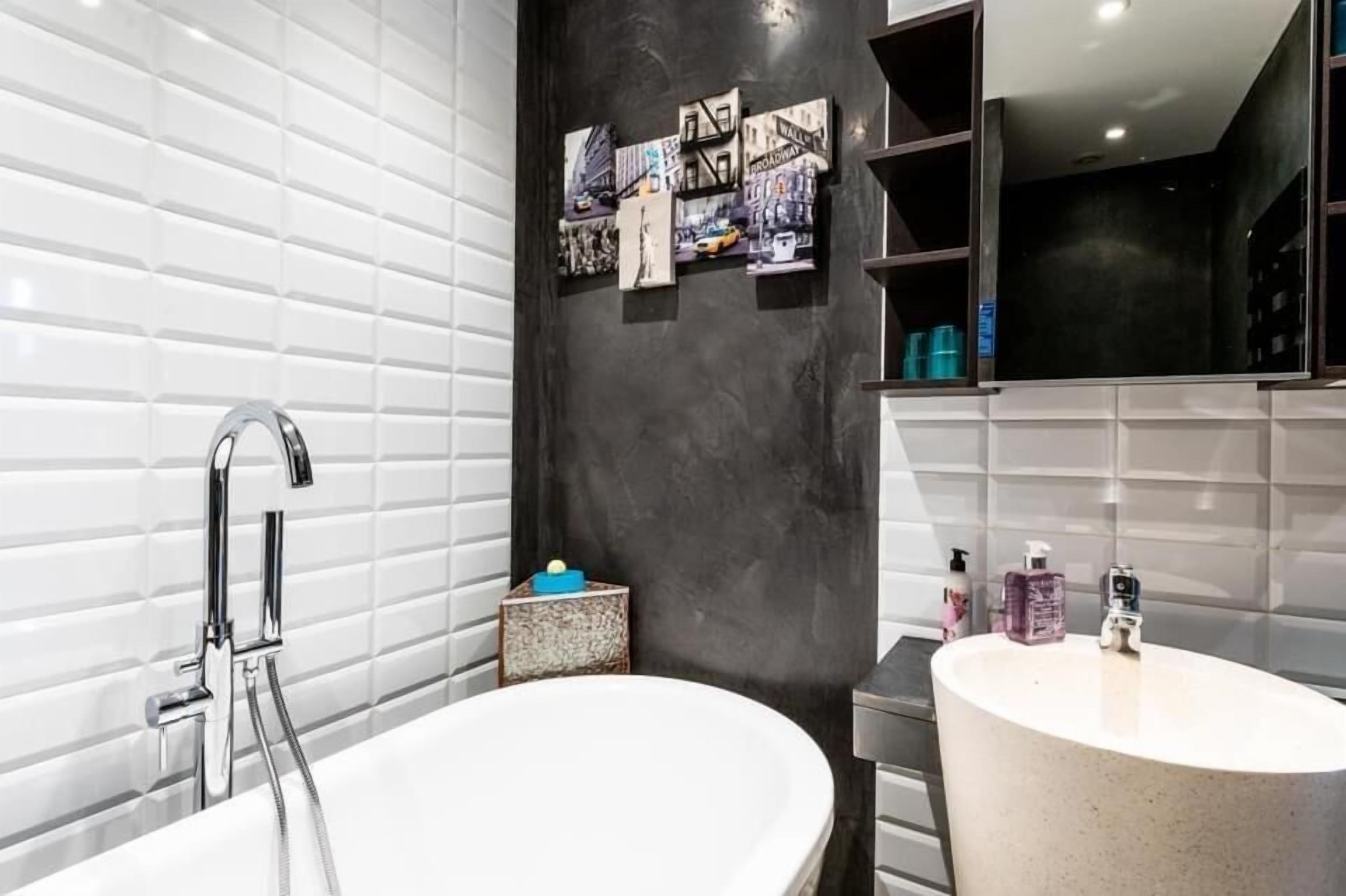 Un baño moderno con una bañera independiente, un tocador con lavamanos y una pared de acento oscura con cuadros enmarcados.