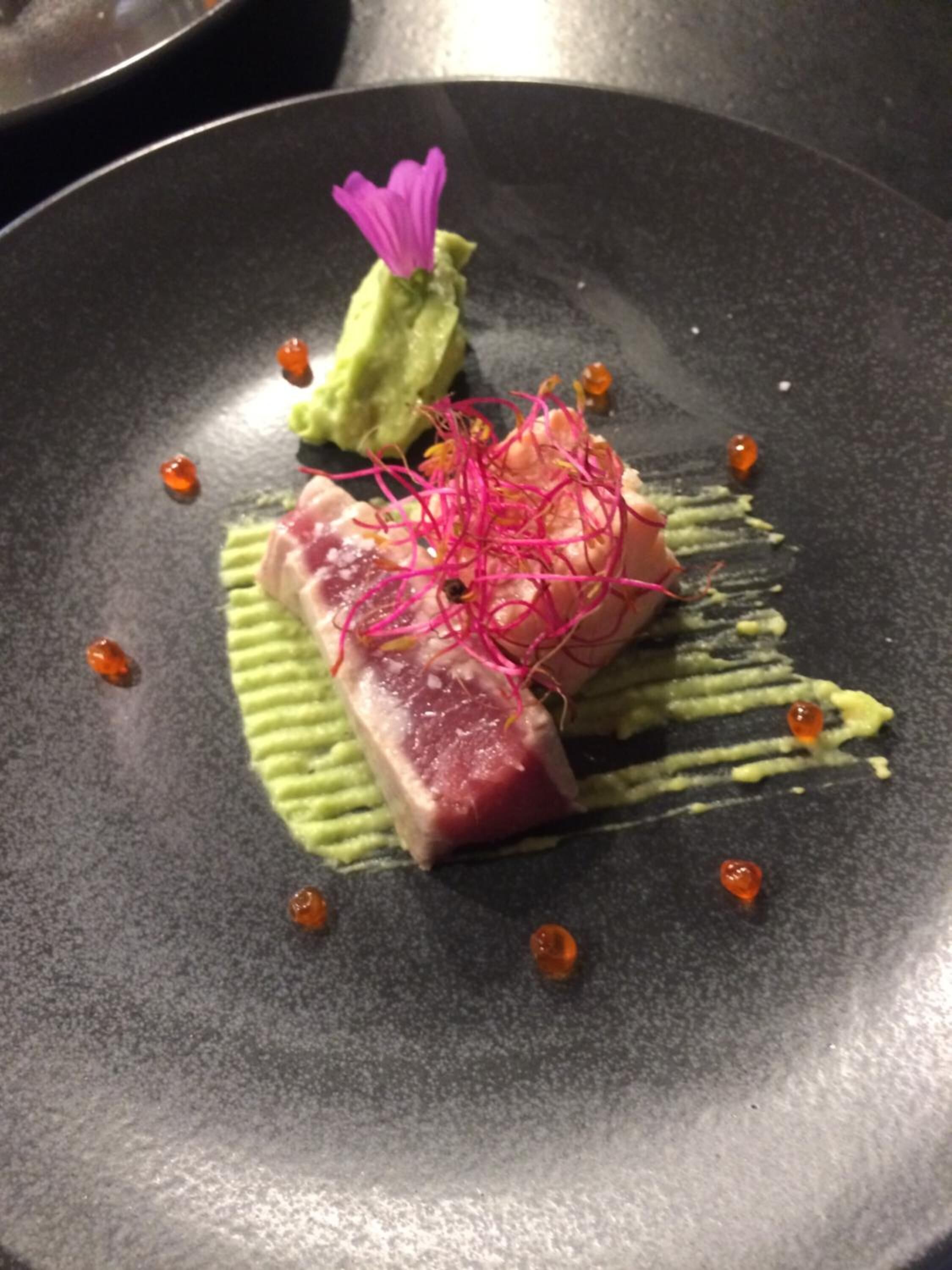 Un plato con una porción de carne, aguacate y una flor morada.