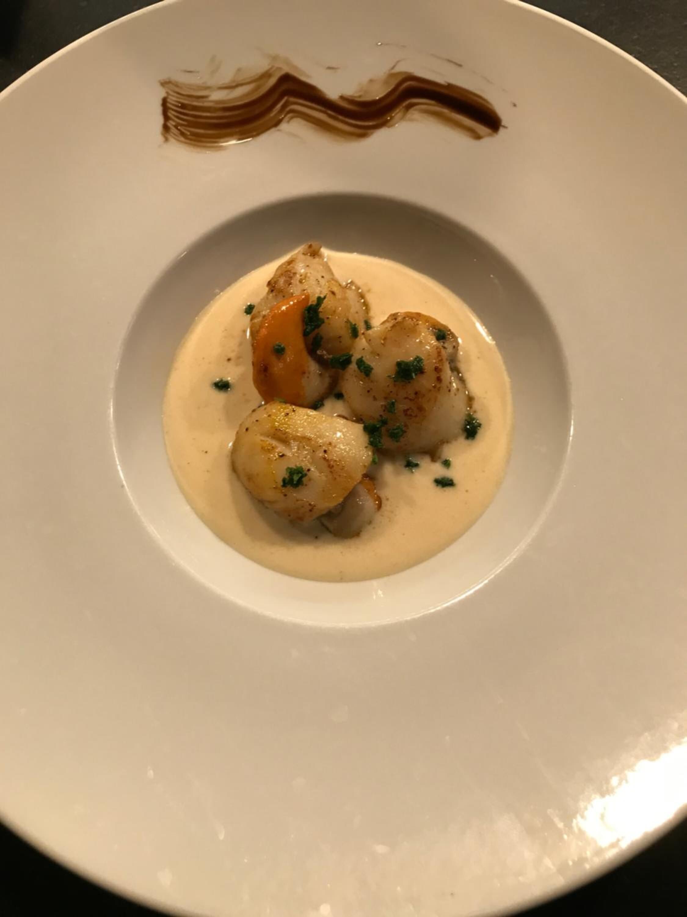 Un plato de vieiras con salsa cremosa, adornado con hierbas.