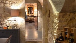 Una habitación con paredes de piedra, un barril de madera, una mesa con lámpara y una silla.