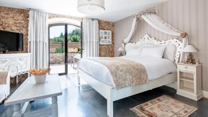 Un dormitorio con pared de piedra, cama con dosel, televisor y vista al exterior.