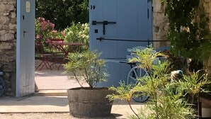 Un arco de piedra que conduce a una puerta azul, rodeado de follaje y una planta en maceta.