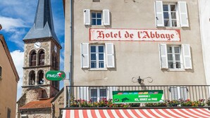 A historic building with a clock tower, a sign for 'Hotel de l'Abbaye', and outdoor seating with a striped awning. - Hôtel Restaurant de l'Abbaye (Sauxillanges)