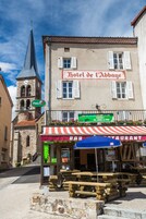 Un edificio histórico con una torre de reloj, un cartel que dice 'Hotel de l'Abbaye' y asientos exteriores con un toldo a rayas.