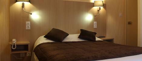 Una habitación de hotel con una cama grande, dos lámparas de noche, un teléfono y una mesita de noche pequeña.