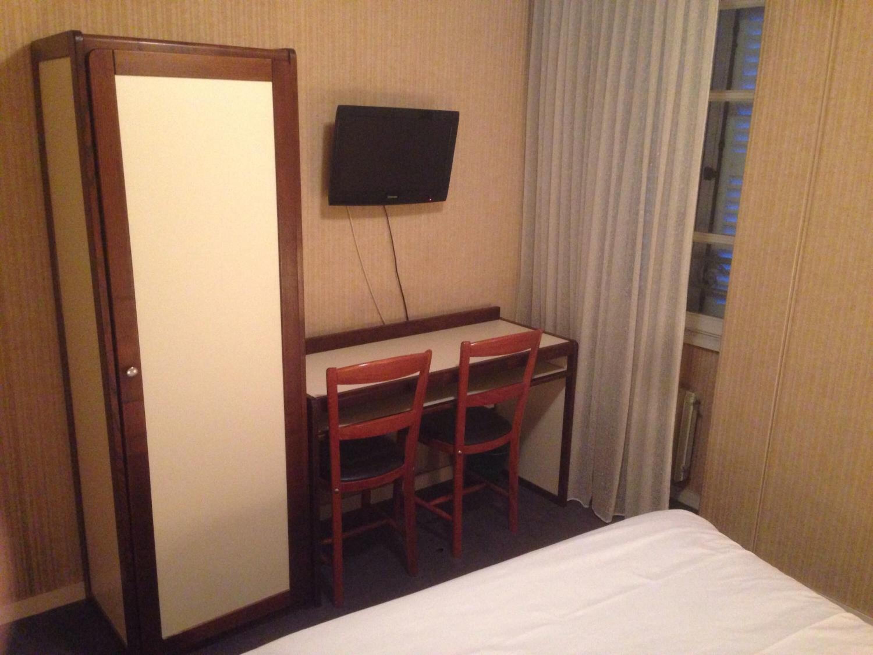 Een hotelkamer met een bed, een bureau, twee stoelen, een televisie en een raam met gordijnen.