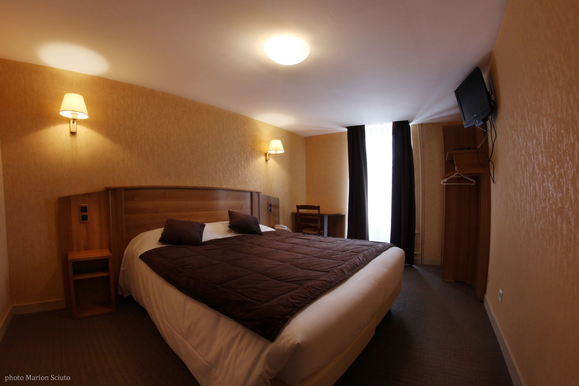 A hotel room with a large bed, two bedside tables, a chair, a TV, and a wardrobe.
