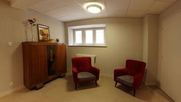 Una habitación con paredes color beige, un armario de madera, dos sillones rojos, una ventana con persianas blancas y una lámpara en el techo.