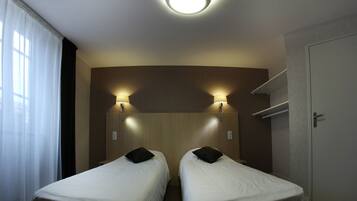 A hotel room with two single beds, a ceiling light, and a door.