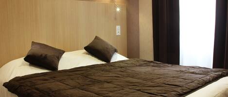 Una habitación de hotel con una cama grande, dos almohadas, una lámpara de pared y una ventana con cortinas.