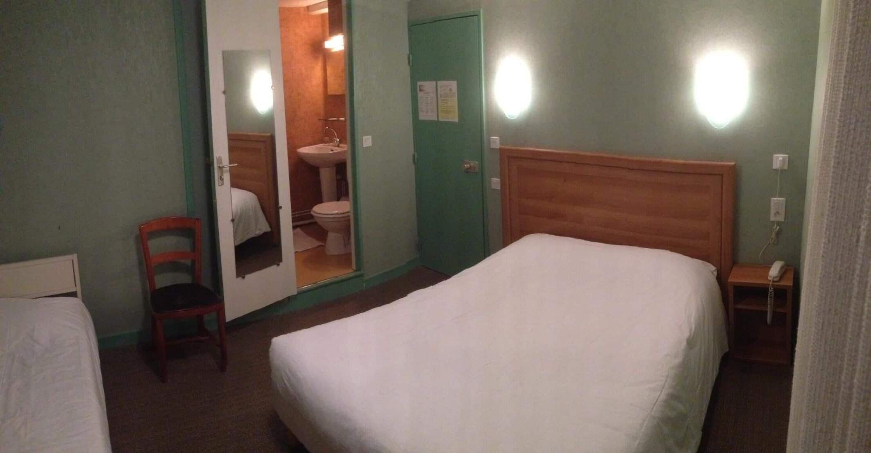 A hotel room with a single bed, a chair, a small table with a phone, and a bathroom visible through an open door.