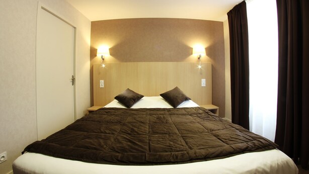 A hotel room with a large bed, two wall-mounted lights, and a window with curtains. - Hôtel Restaurant de l'Abbaye (Sauxillanges)