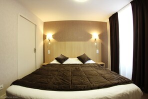 A hotel room with a large bed, two wall-mounted lights, and a window with curtains. - Hôtel Restaurant de l'Abbaye (Sauxillanges)