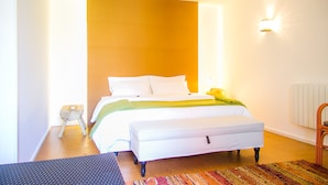 Um quarto com cama, mesa de cabeceira, cadeira, janela e luminária na parede.