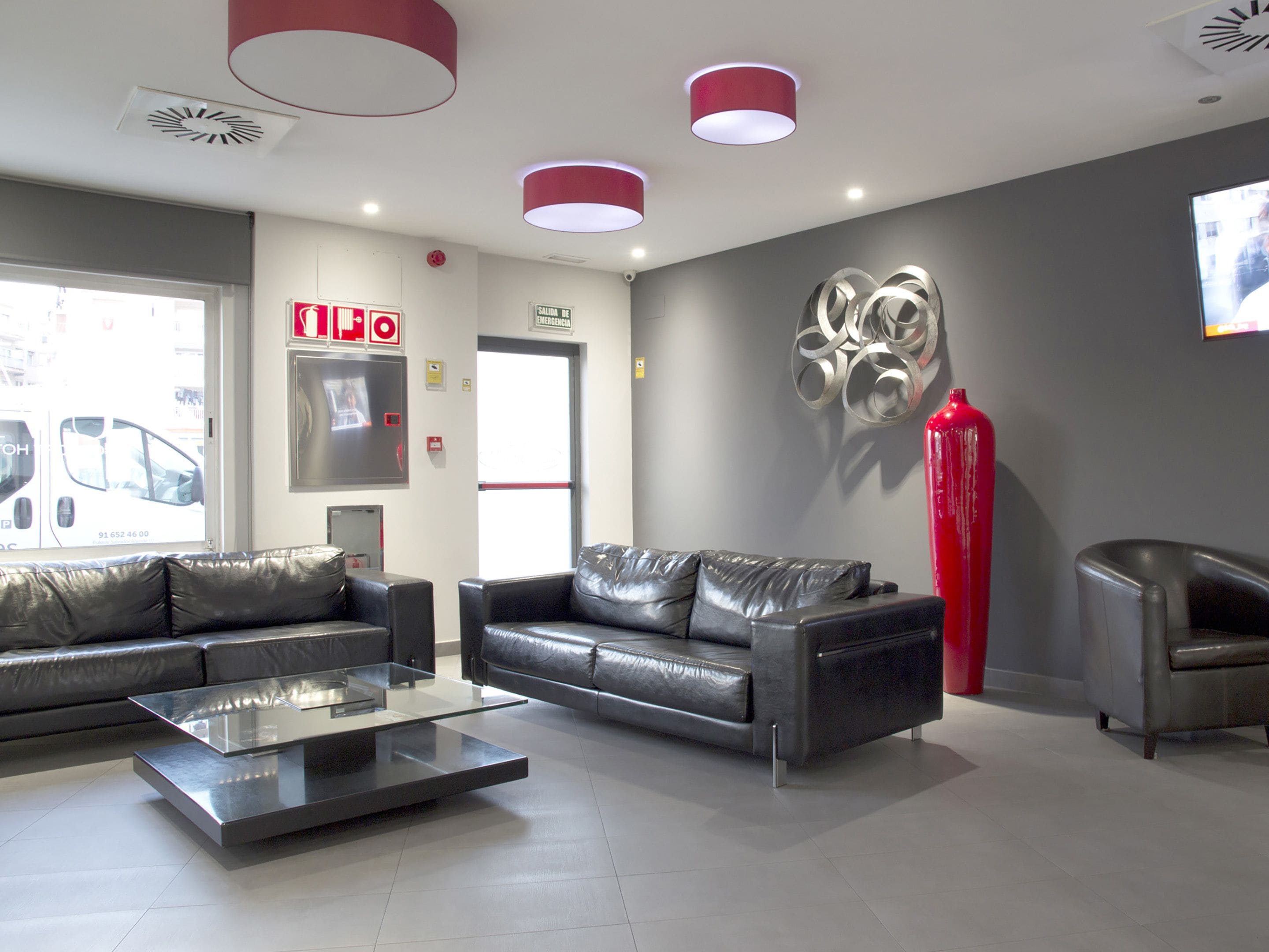 Un espace d’accueil moderne avec des canapés en cuir, une table basse en verre et une sculpture rouge.
