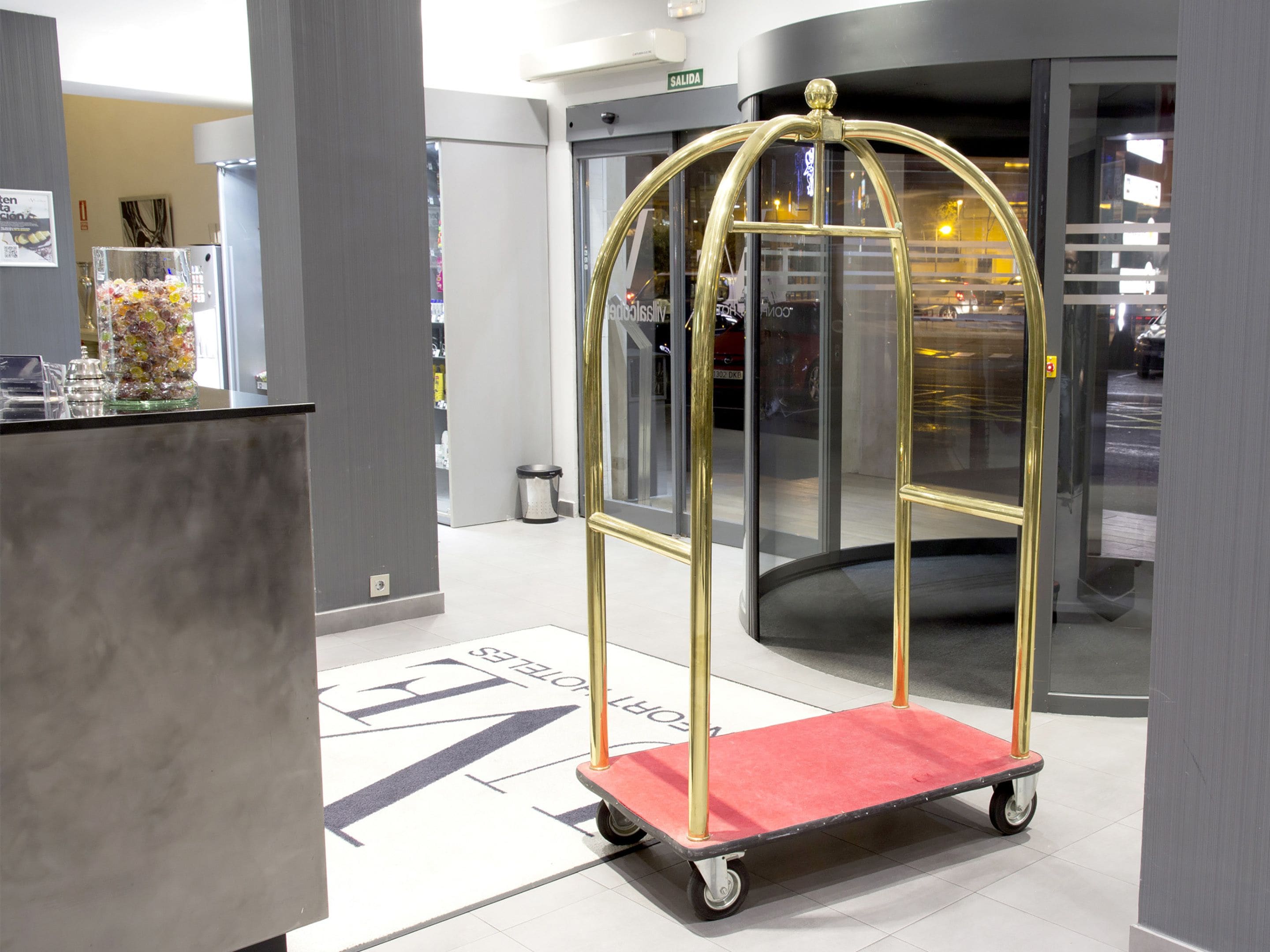 Een hotel lobby met een receptiebalie, een glazen vitrine en een lift met gouden lijst.