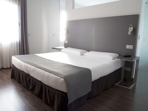 Una habitación de hotel moderna con una cama grande, mesitas de noche y una mesilla.