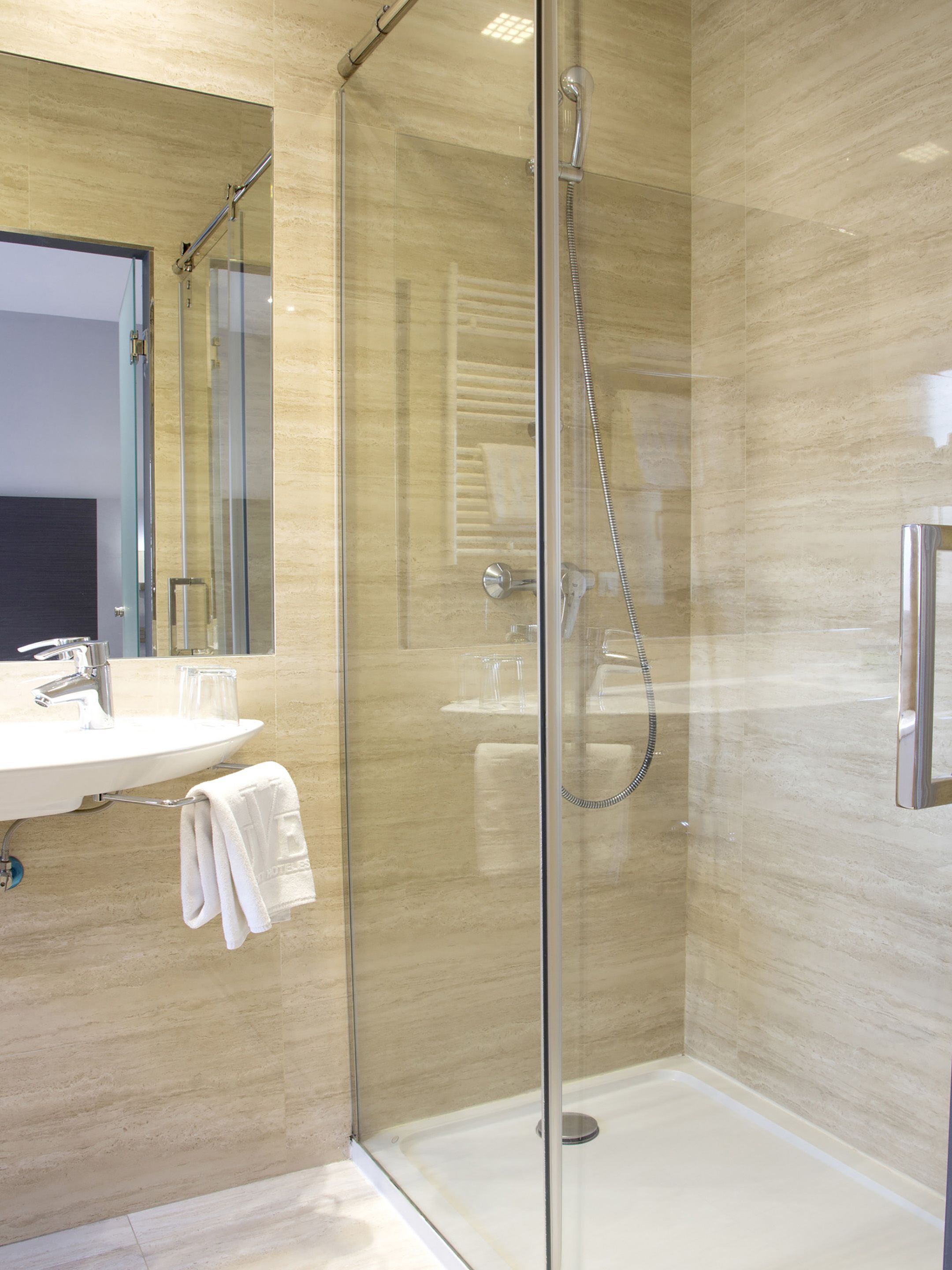 Un baño moderno con ducha de mampara de vidrio, lavamanos y un perchero para toallas.
