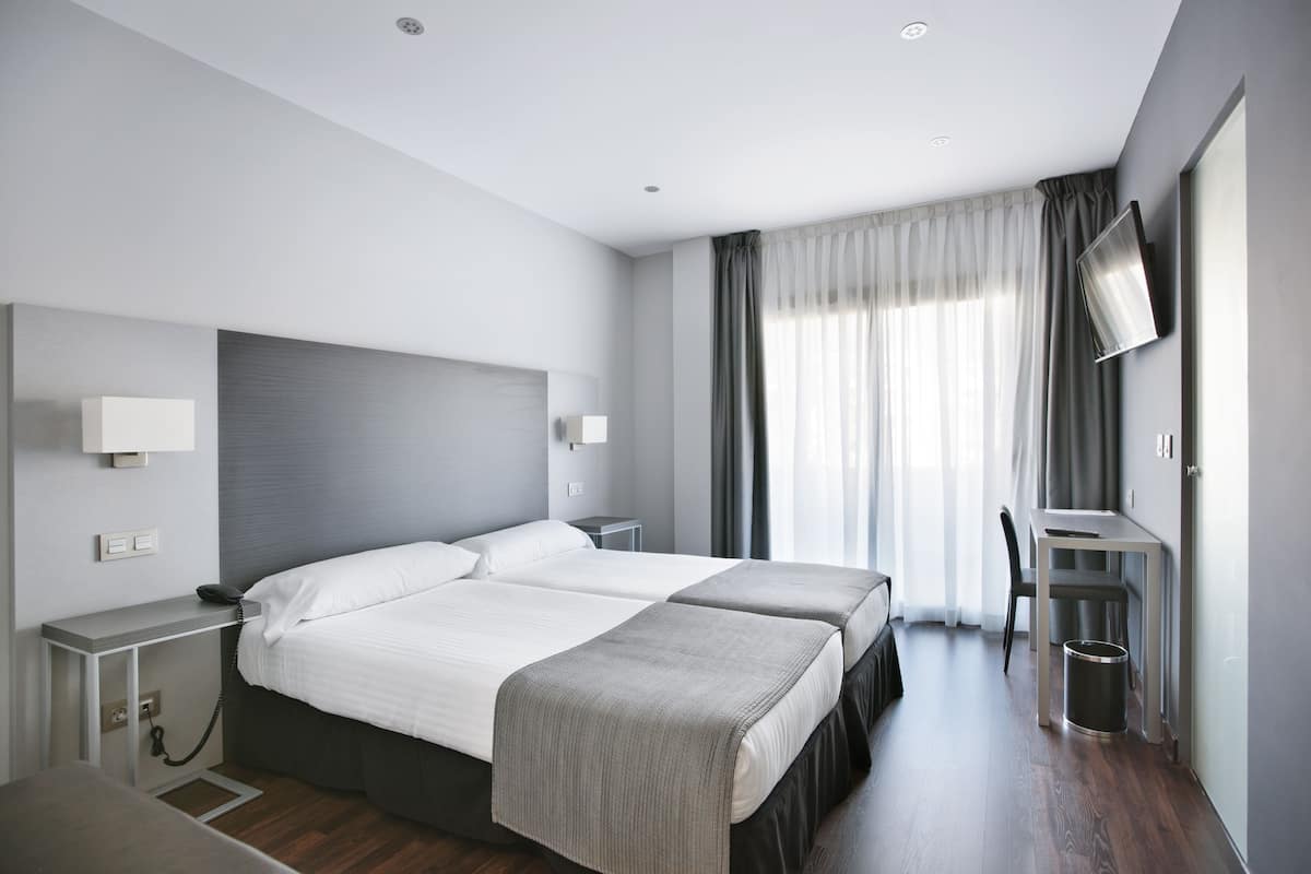 Una camera d'albergo con un letto, comodini, una scrivania, una sedia, una TV e una finestra con tende.