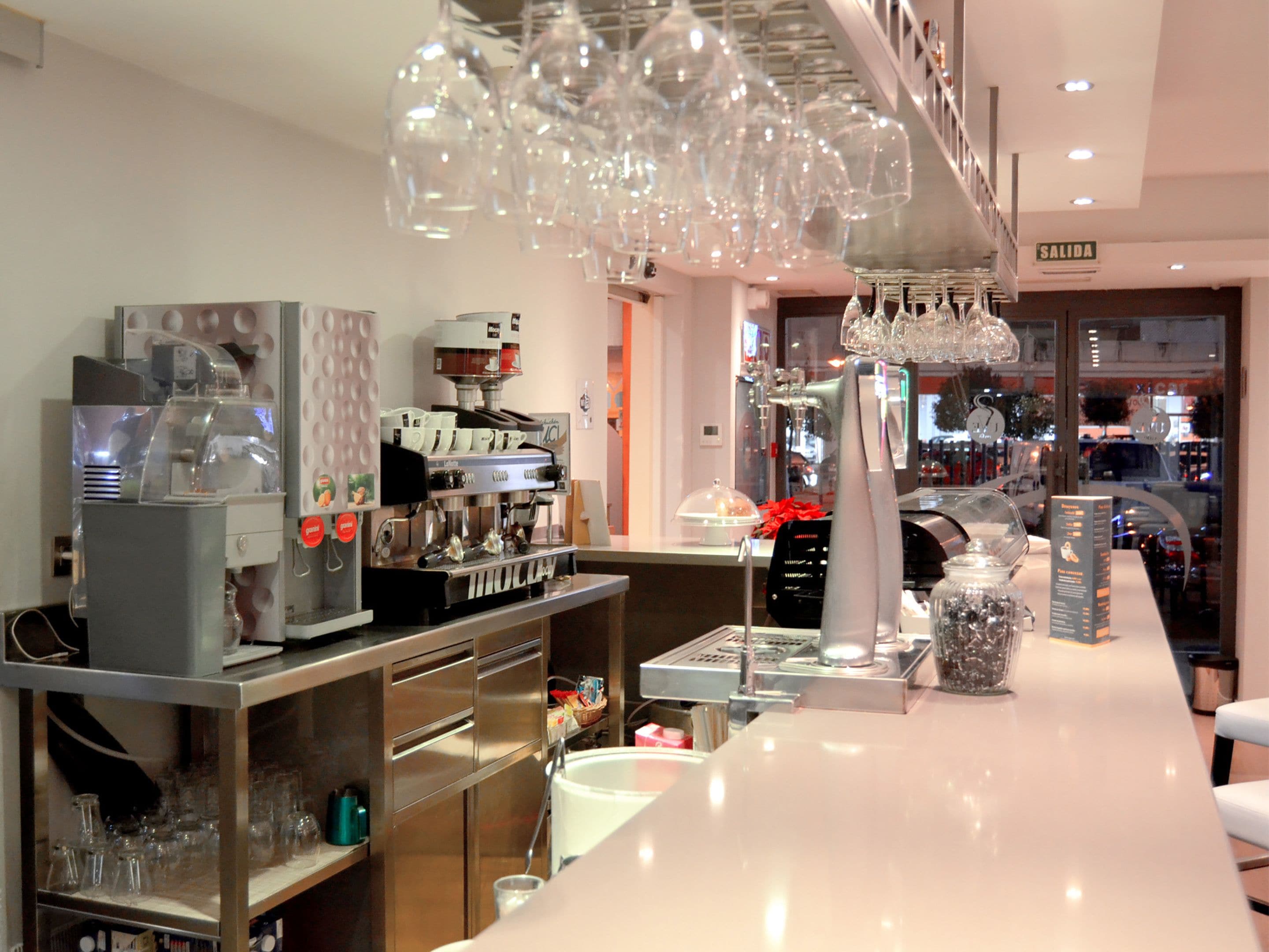 Interior de una cafetería moderna con una máquina de café, vasos y mostrador.