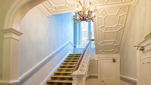 A grand staircase with a white balustrade, a chandelier, and a blue wall. - Balcary House Hotel (Hawick)