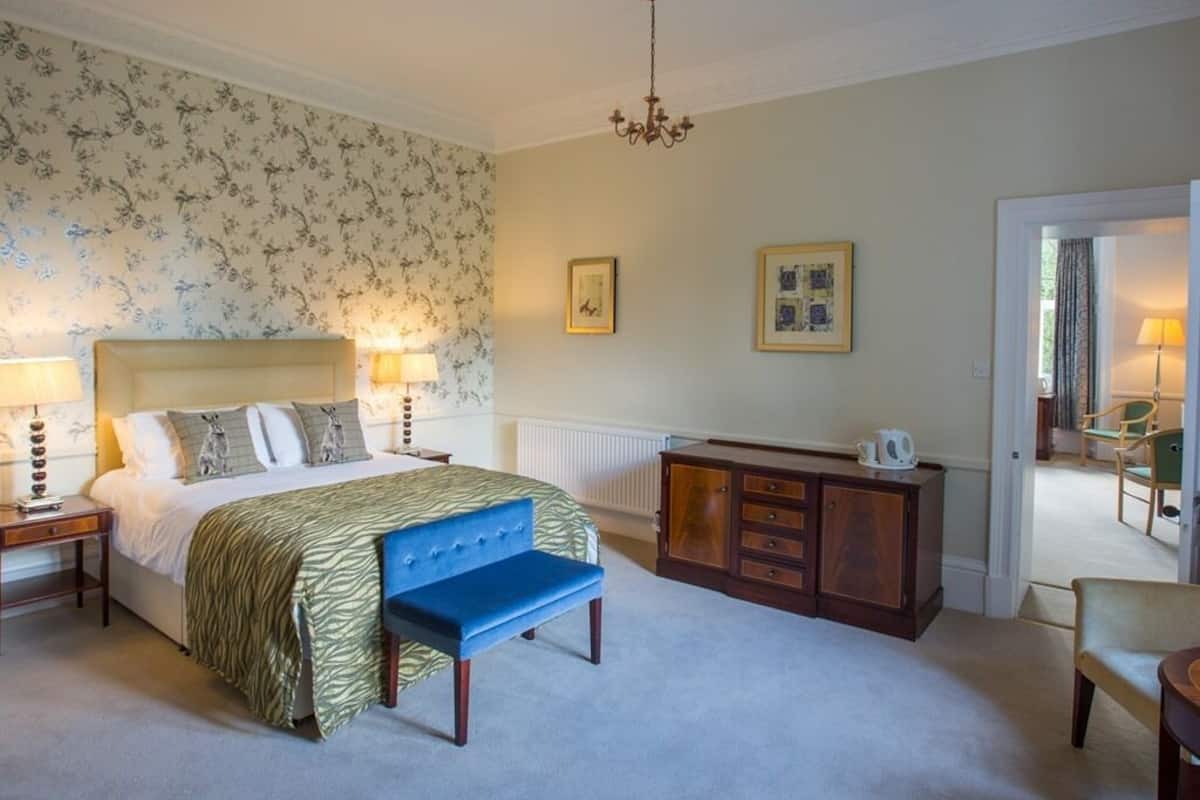 A bedroom with a bed, bedside tables, a bench, a dresser, and a chandelier.