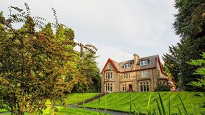 A large stone building with a red roof, surrounded by well-manicured lawns and trees. - Balcary House Hotel (Hawick)