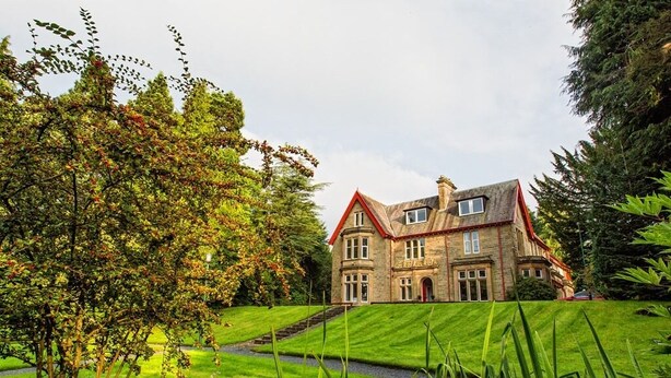 A large stone building with a red roof, surrounded by well-manicured lawns and trees. - Balcary House Hotel (Hawick)