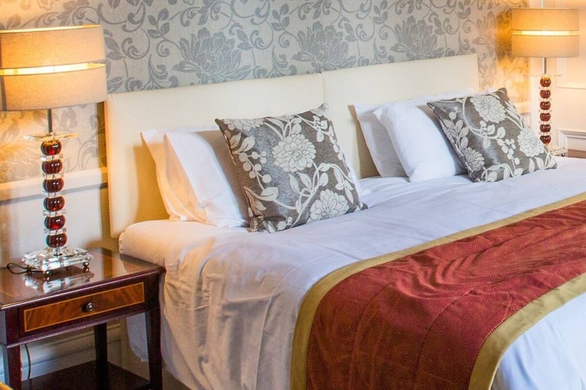 A neatly made bed with a red blanket, two bedside lamps, and floral-patterned pillows.