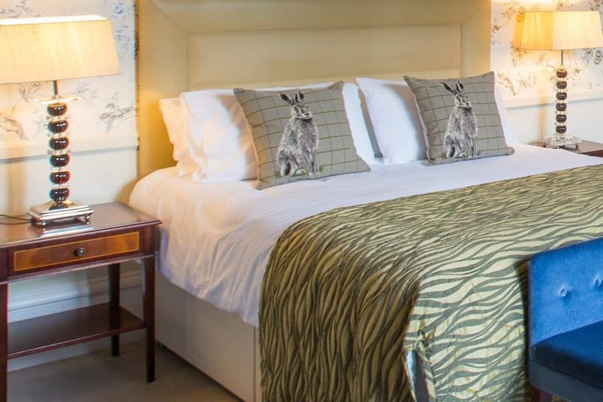 A neatly made bed with a zebra-patterned blanket, two pillows with a rabbit design, and a headboard.