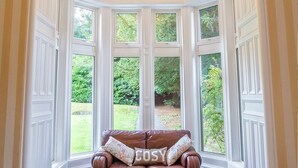 A corner room with a brown leather sofa and a window with a view of greenery. - Balcary House Hotel (Hawick)