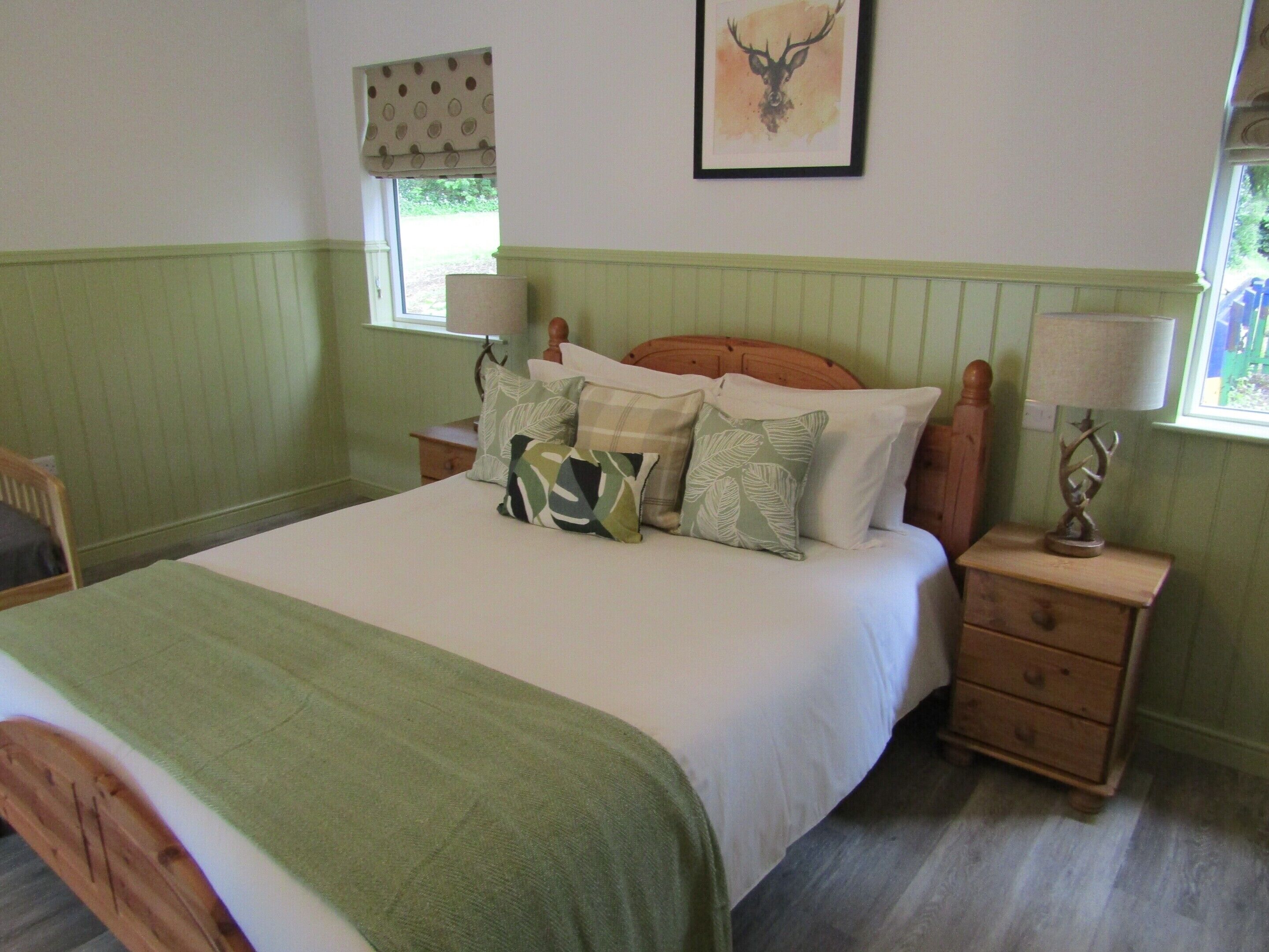 A bedroom with a bed, pillows, a nightstand, a lamp, and a framed deer head on the wall.