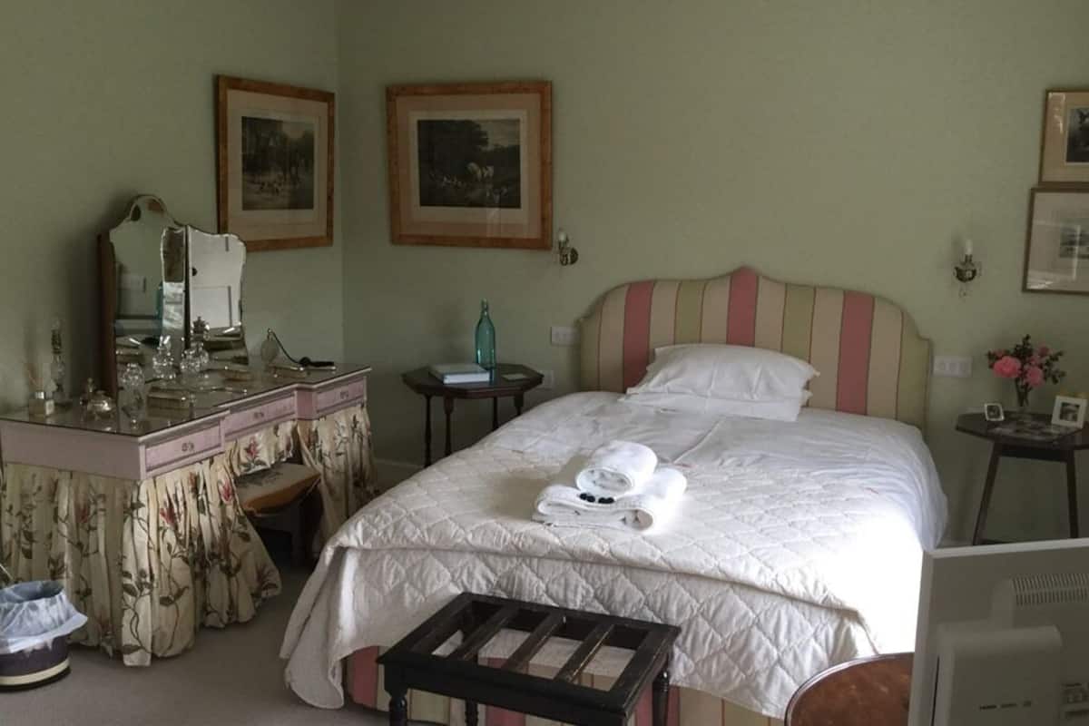 A hotel room with a bed, a vanity with a mirror, a dresser, and framed pictures on the walls.