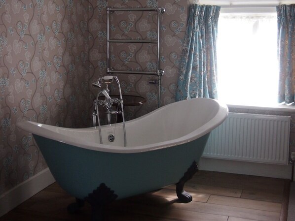 Un baño con una bañera independiente, un perchero y una ventana con cortinas.