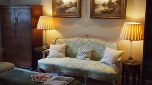 A cozy room with a green upholstered sofa, two lamps, a wooden cabinet, and two framed paintings on the wall. - Clare Cottage (Sherborne)