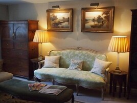 Un cuarto acogedor con un sofá tapizado en verde, dos lámparas, un aparador de madera y dos cuadros enmarcados en la pared.