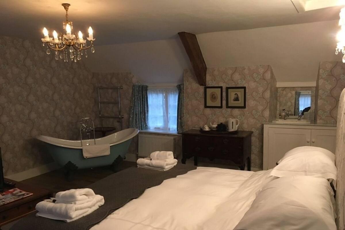 A hotel room with a large bed, a bathtub, a vanity with a mirror, and a chandelier.