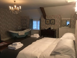 Una habitación de hotel con una cama grande, una bañera, un tocador con espejo y un candelabro.