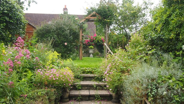 A stone staircase leading to a wooden pergola surrounded by lush greenery and flowering plants. - Clare Cottage (Sherborne)