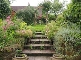 Una escalera de piedra que lleva a una pérgola de madera rodeada de exuberante follaje y plantas en flor.