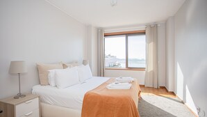 Camera d'hotel moderna con un letto grande, un comodino, una lampada e vista sulla città attraverso una grande finestra.